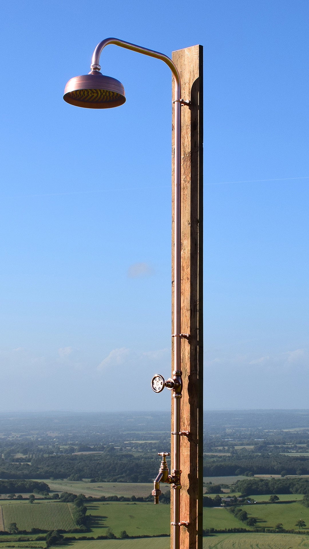 Full view of Quara copper cold outdoor shower with garden tap. photographed next to a stunning view of Brighton countryside.