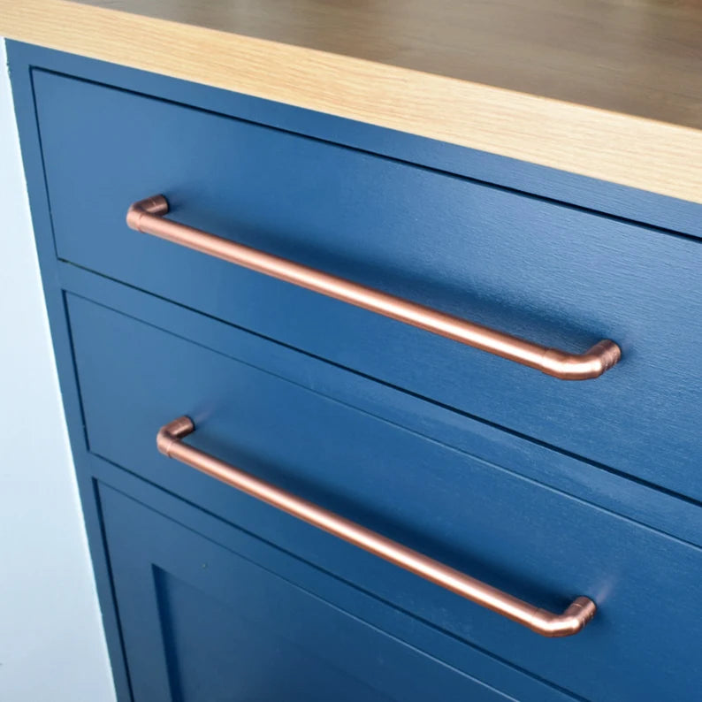 Long copper handle on blue cabinet