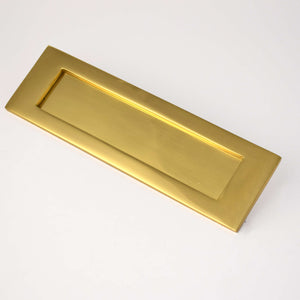 Polished brass letter plate on plain background